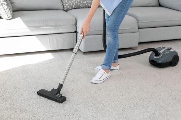 Person vacuuming a light-colored carpet in a modern living room