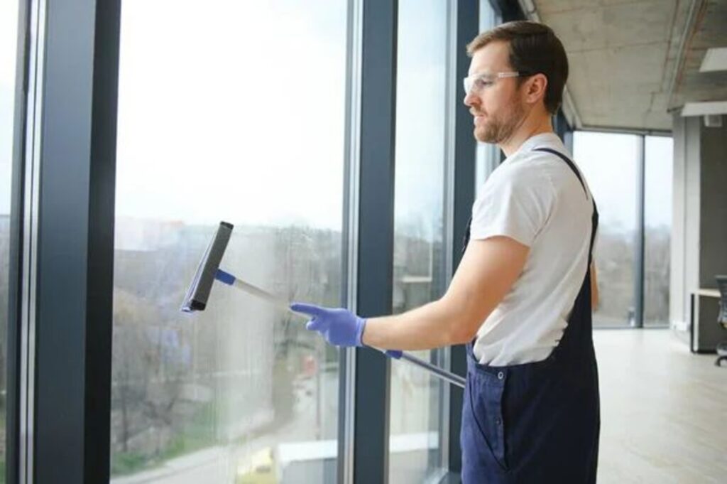 Professional cleaner wearing gloves and goggles cleaning large glass windows with a squeegee